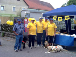Gruppenfoto mit allen Betreuern und ihren Führhunden neben dem Infostand. Technischer Hinweis: In der Bildmitte befindet sich ein Hotspot. Wenn Sie darauf klicken, wird das bild vergrößert dargestellt. 